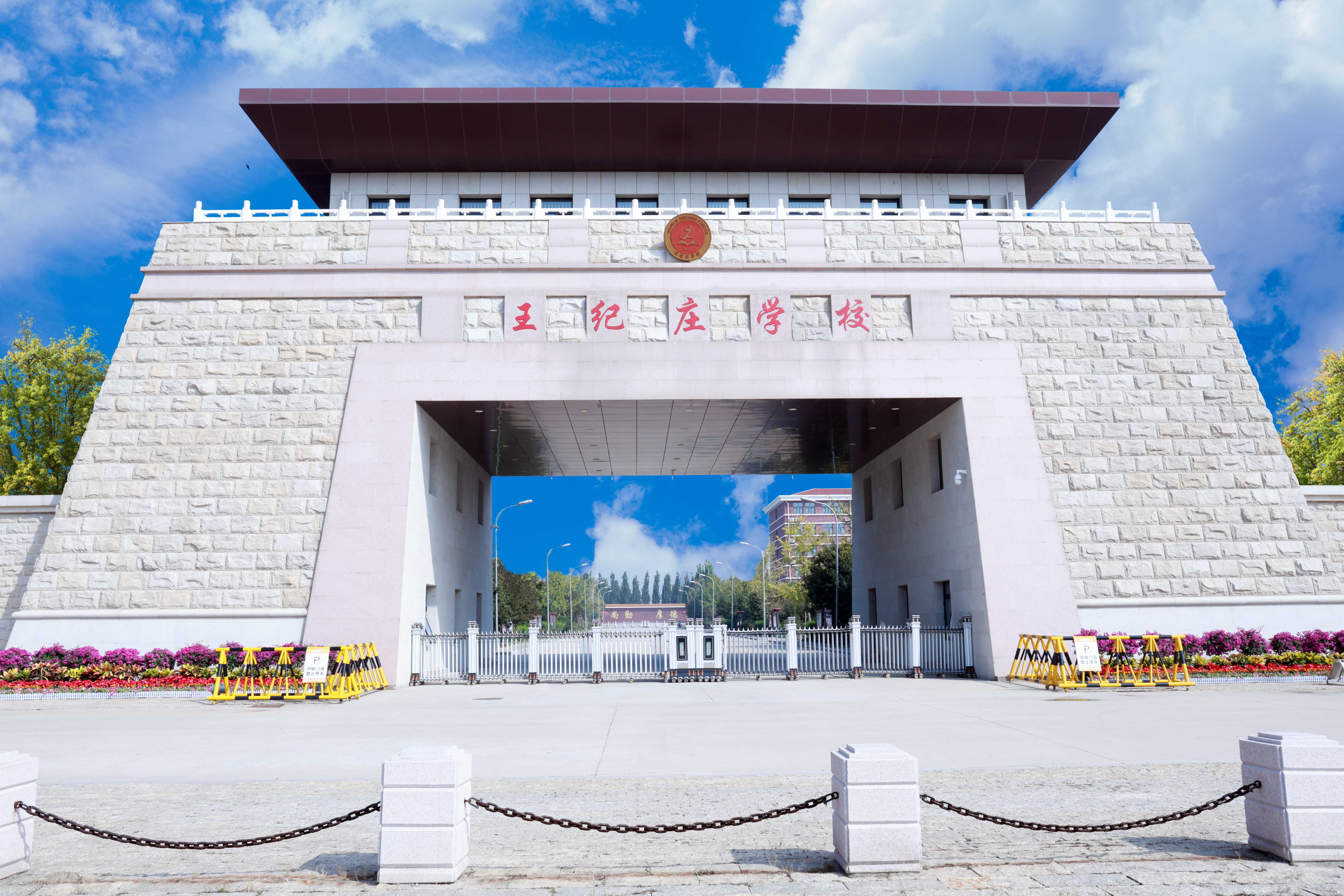 红砖外墙、多层结构的教学楼，楼顶醒目“王纪庄学校”字样，窗框为绿色，外立面整齐排列空调外机，前方为红色塑胶操场，整体布局规整，体现标准化校园建设。